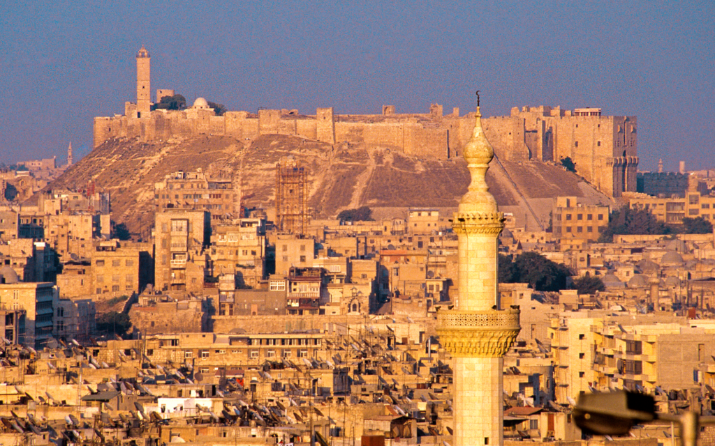 The Citadel of Aleppo, on the left the minaret of its Great Mosque (Maqam Ibrahim) – view from the west, in the foreground is the minaret of the Jamiʿ Sayf ad-Dawla, Peter Heiske (CC-BY-NC-ND)